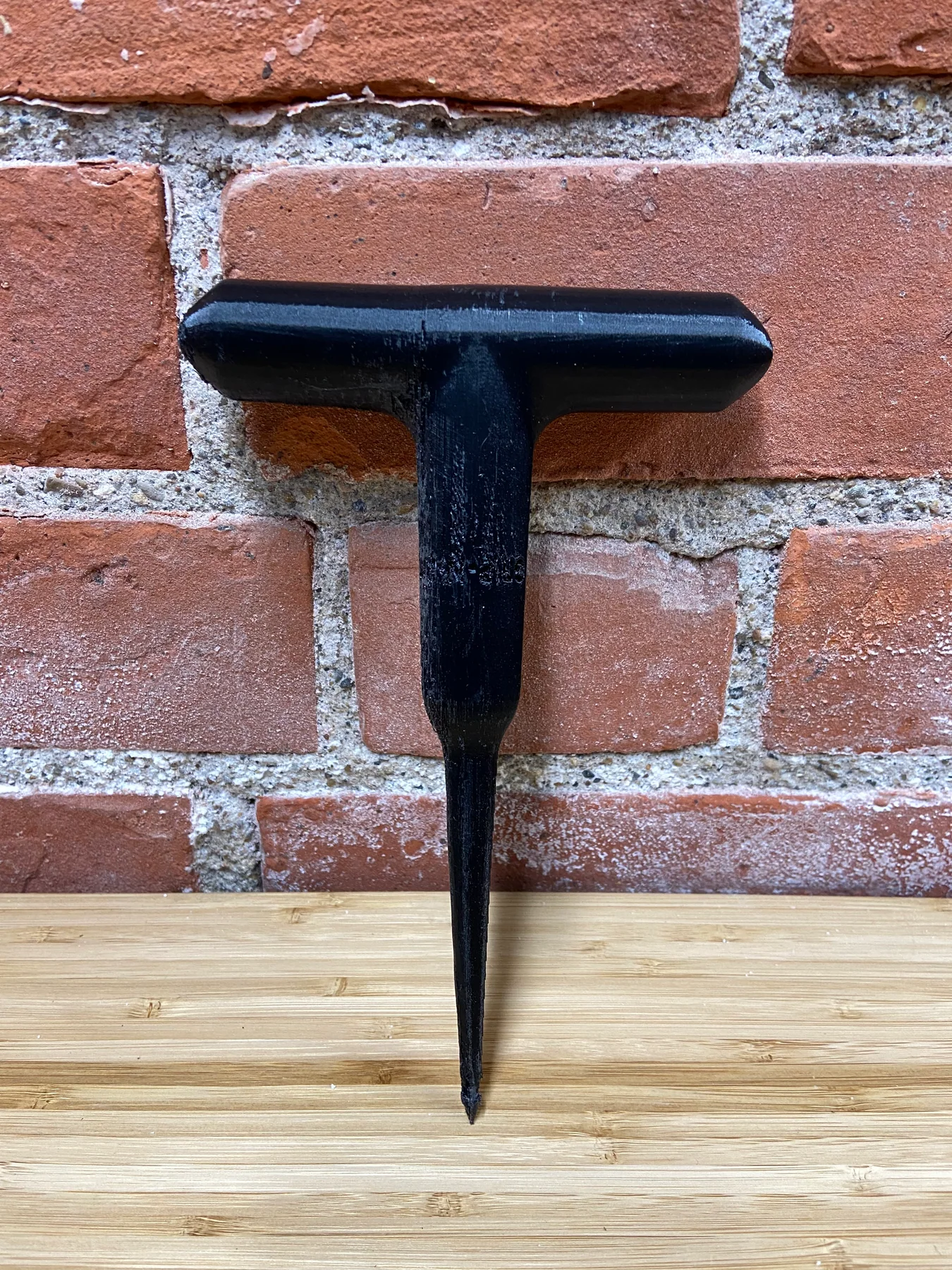 First printed prototype of the T-handle tool resting against a brick wall