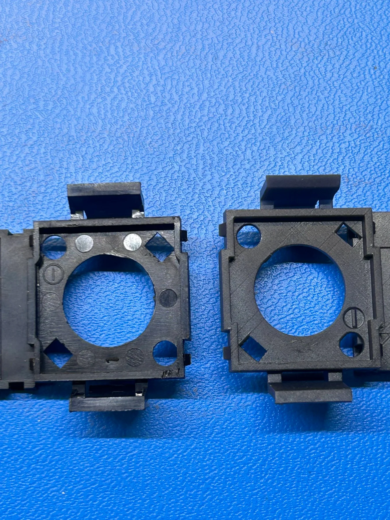 Original battery tray component next to the SLA-printed prototype on a work mat